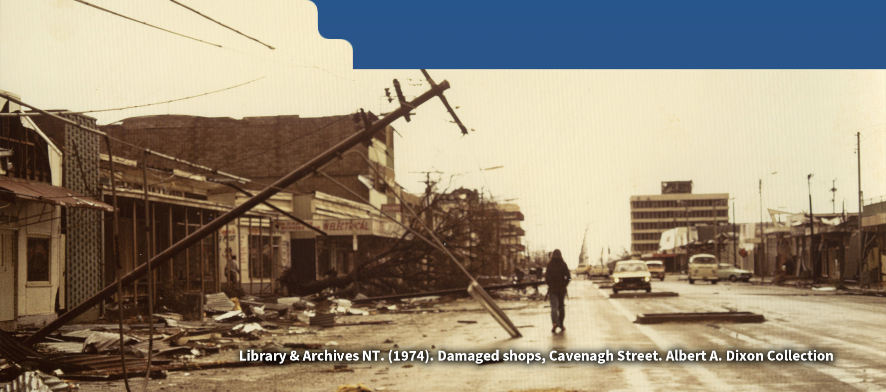 Photo showing extensive destruction in Darwin caused by Cyclone Tracy, a man walking in rubble and detris on the street